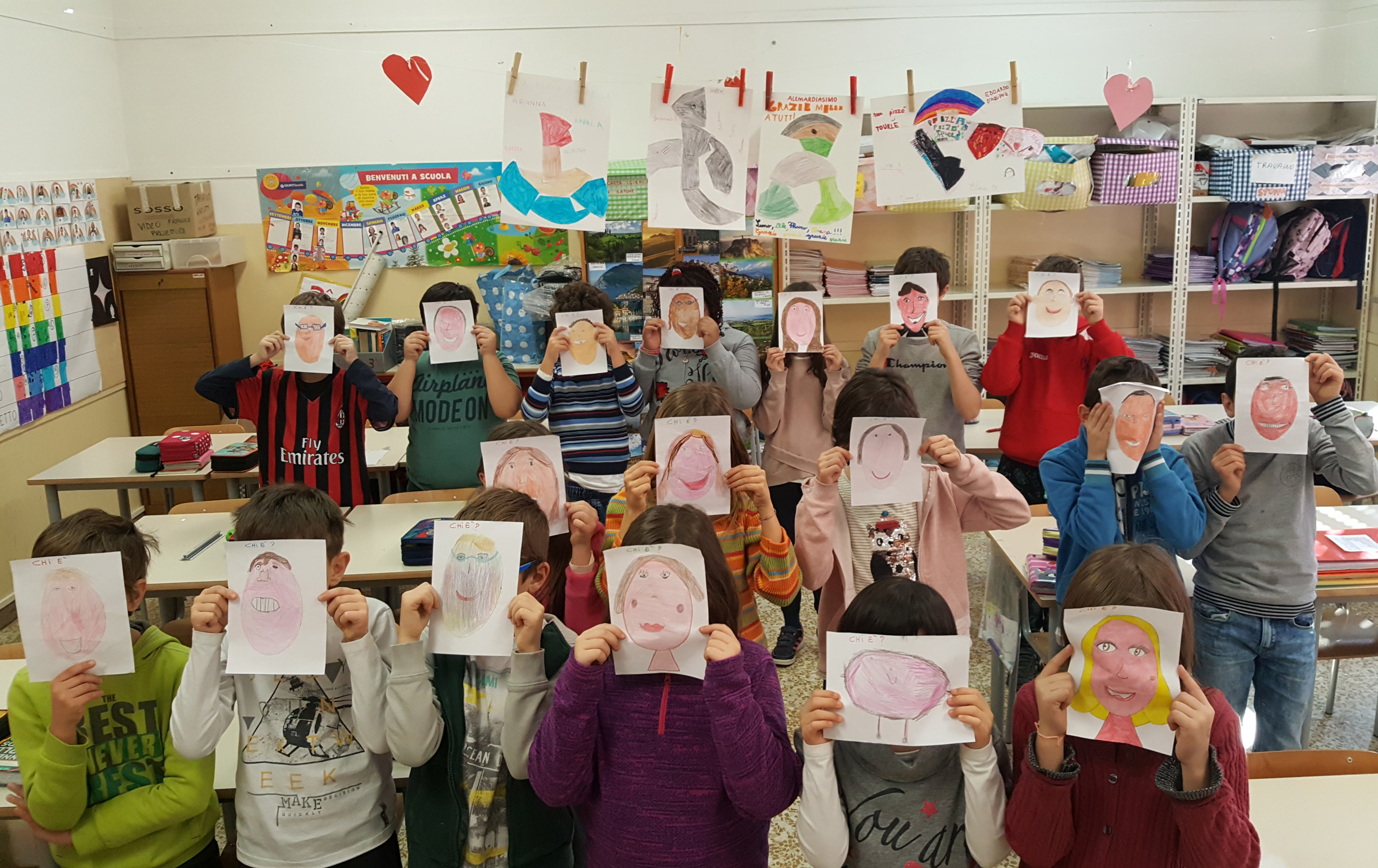 Classe di bambini che si coprono il volto con un disegno rappresentante il proprio viso