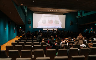 foto di teatro con numerose persone a sedere e sul palco